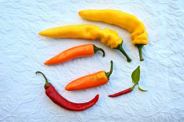 Beyaz, dokulu bir masa örtüsü üzerinde duran parlak renkli kırmızı, turuncu ve sarı biberlerden oluşan bir biberin tepetaklak yatağı. Baharatlı mutfak, yemek pişirme ve canlı yemek kontrastı temaları için ideal..