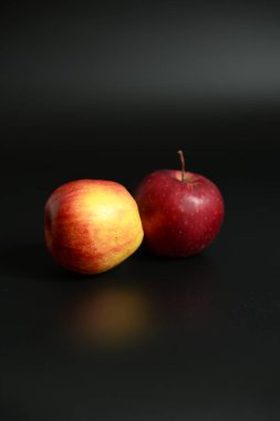 İki taze, olgun elma (biri kırmızı, biri sarı / kırmızı) siyah bir yüzey üzerinde dinleniyor. Minimalist tasarım sağlıklı yeme ve kontrast vurguluyor.
