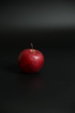 Tek, taze, olgun kırmızı bir elma siyah bir yüzeyde duruyor. Minimalist tasarım sağlıklı beslenmeyi ve katı renk kontrastını vurguluyor. Mükemmel kopyalama alanı.