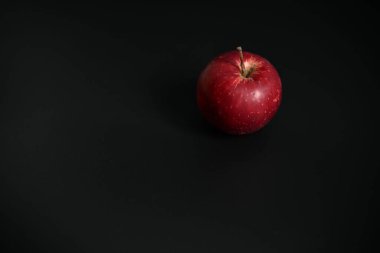 Tek, taze, olgun kırmızı bir elma siyah bir yüzeyde duruyor. Minimalist tasarım sağlıklı beslenmeyi ve katı renk kontrastını vurguluyor. Mükemmel kopyalama alanı.