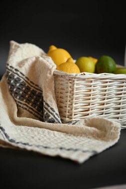 Limonlar ve limonlar dokuma sepetinde desenli keten bir mutfak havlusuyla sarılı. Koyu bir arkaplan yerine doğal dokuya odaklan.