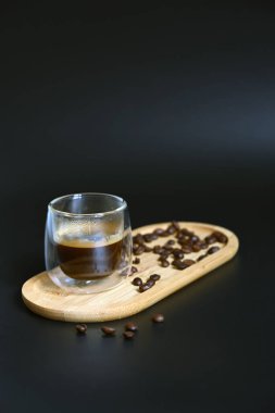 Espresso kahvesi, küçük tahta bir kürek üzerinde cam bir fincanda, kırsal bir arka planda kahve çekirdekleri ile çevrili..