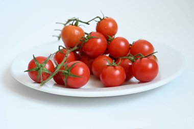 Organik olgun vişneli domatesler dalda. Beyaz tabakta taze mevsimlik sebzeler. Mutfak ve sağlık projeleri için yüksek kaliteli gıda fotoğrafçılığı.