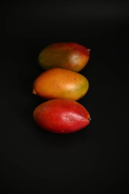 Esmer arka planda üç renkli organik mangodan oluşan kaliteli bir stüdyo çekimi. Gıda ambalajı, sağlıklı yaşam tarzı tasarımı ve mutfak kavramları için ideal..