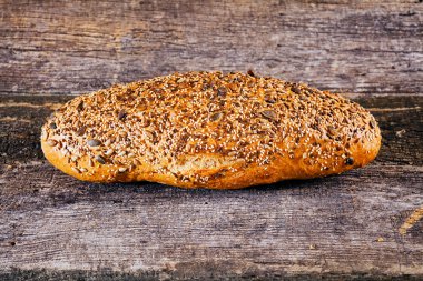 Çeşitli tohumlarla kaplı ev yapımı ekmek, eski ahşap masada.
