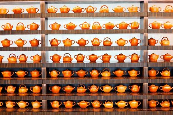 Mağazadaki raflarda çeşitli kil çaydanlıklar var.