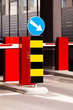 Bariyer ve zorunlu yol işareti ile park girişi, arka planda bina