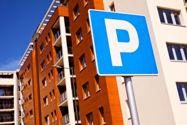 Mavi park tabelasına yakın, arka planda kahverengi bina.