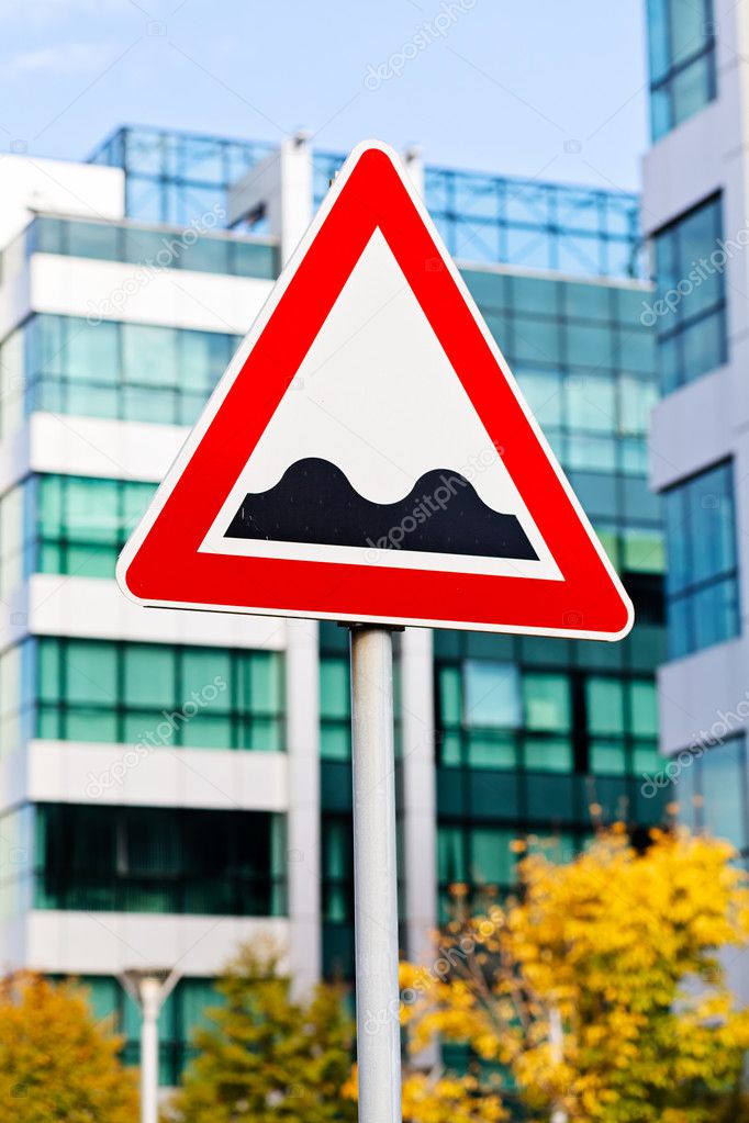 Red and white triangle bumpy road sign with business building in background