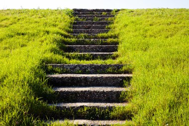 Arka planda gökyüzü olan küçük bir tepede çimenlerdeki taş yığınları; aşağıdan görünüm