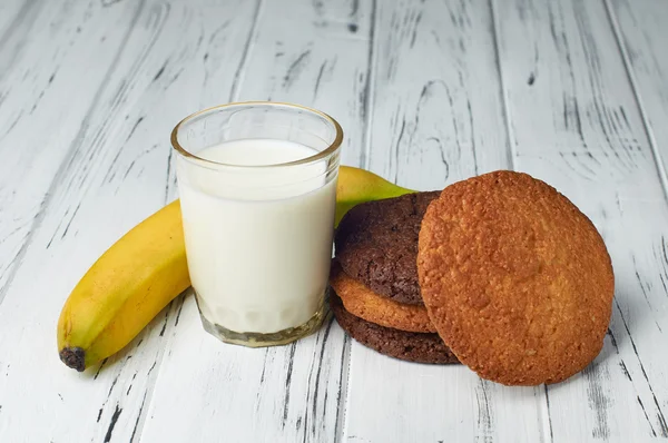 Молоко, банан і печиво на красивому білому дерев'яному столі . — стокове фото