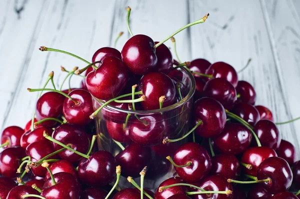 A lot of sweet cherry and a transparent glass on a white table. Stock Picture
