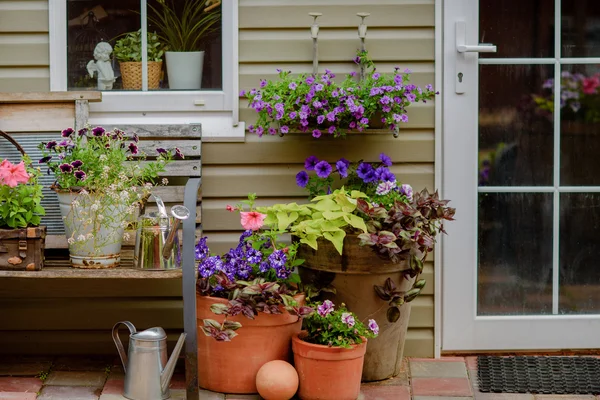 Hermoso porche decorado de una casa privada, flores de colores en grandes ollas de barro, banco vintage, inventario vintage . — Foto de Stock