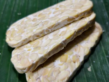 Taze dilimlenmiş tempeh muz yaprağında geleneksel Endonezya yemeklerini ve sağlıklı bitki temelli protein konseptini gösteriyor. Temiz yemek, vegan yaşam tarzı ve doğal mutfak.