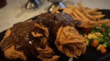 Bol tuzlu sos soslu kızarmış tavuk, yanında patates kızartması ve karışık sebze, restoran menüsü ve yemek reklamı için mükemmel bir konfor yemeği.