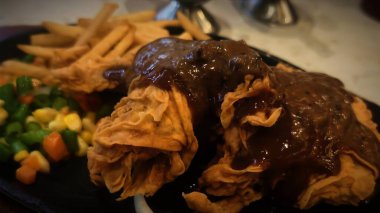 Bol tuzlu sos soslu kızarmış tavuk, yanında patates kızartması ve karışık sebze, restoran menüsü ve yemek reklamı için mükemmel bir konfor yemeği.