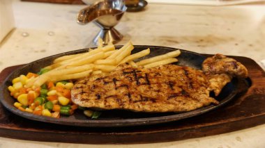 Kızarmış patates kızartması ve renkli taze sebzelerle servis edilen sulu ızgara tavuk bifteği restoran menüsü, yemek reklamı ve ticari mutfak içeriği için mükemmel.