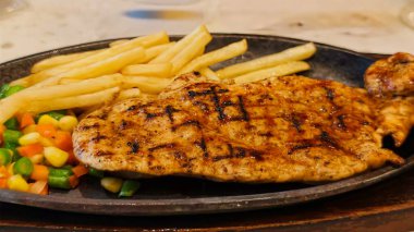 Kızarmış patates kızartması ve renkli taze sebzelerle servis edilen sulu ızgara tavuk bifteği restoran menüsü, yemek reklamı ve ticari mutfak içeriği için mükemmel.