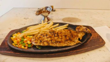 Kızarmış patates kızartması ve renkli taze sebzelerle servis edilen sulu ızgara tavuk bifteği restoran menüsü, yemek reklamı ve ticari mutfak içeriği için mükemmel.