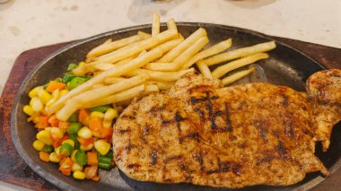 Kızarmış patates kızartması ve renkli taze sebzelerle servis edilen sulu ızgara tavuk bifteği restoran menüsü, yemek reklamı ve ticari mutfak içeriği için mükemmel.