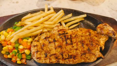 Kızarmış patates kızartması ve renkli taze sebzelerle servis edilen sulu ızgara tavuk bifteği restoran menüsü, yemek reklamı ve ticari mutfak içeriği için mükemmel.
