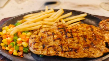 Kızarmış patates kızartması ve renkli taze sebzelerle servis edilen sulu ızgara tavuk bifteği restoran menüsü, yemek reklamı ve ticari mutfak içeriği için mükemmel.