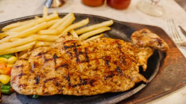 Kızarmış patates kızartması ve renkli taze sebzelerle servis edilen sulu ızgara tavuk bifteği restoran menüsü, yemek reklamı ve ticari mutfak içeriği için mükemmel.