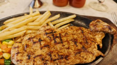 Kızarmış patates kızartması ve renkli taze sebzelerle servis edilen sulu ızgara tavuk bifteği restoran menüsü, yemek reklamı ve ticari mutfak içeriği için mükemmel.