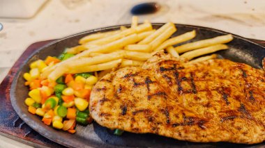 Kızarmış patates kızartması ve renkli taze sebzelerle servis edilen sulu ızgara tavuk bifteği restoran menüsü, yemek reklamı ve ticari mutfak içeriği için mükemmel.