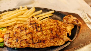 Kızarmış patates kızartması ve renkli taze sebzelerle servis edilen sulu ızgara tavuk bifteği restoran menüsü, yemek reklamı ve ticari mutfak içeriği için mükemmel.