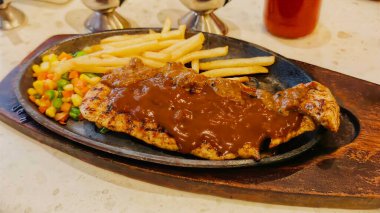 Kızarmış patates kızartması ve renkli taze sebzelerle servis edilen sulu ızgara tavuk bifteği restoran menüsü, yemek reklamı ve ticari mutfak içeriği için mükemmel.