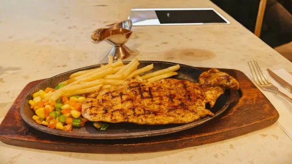 Kızarmış patates kızartması ve renkli taze sebzelerle servis edilen sulu ızgara tavuk bifteği restoran menüsü, yemek reklamı ve ticari mutfak içeriği için mükemmel.