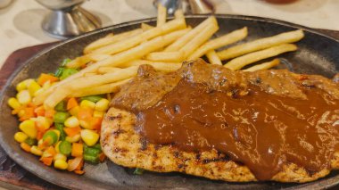 Kızarmış patates kızartması ve renkli taze sebzelerle servis edilen sulu ızgara tavuk bifteği restoran menüsü, yemek reklamı ve ticari mutfak içeriği için mükemmel.