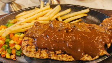 Kızarmış patates kızartması ve renkli taze sebzelerle servis edilen sulu ızgara tavuk bifteği restoran menüsü, yemek reklamı ve ticari mutfak içeriği için mükemmel.