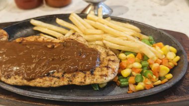 Kızarmış patates kızartması ve renkli taze sebzelerle servis edilen sulu ızgara tavuk bifteği restoran menüsü, yemek reklamı ve ticari mutfak içeriği için mükemmel.
