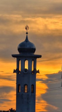 Gün batımında caminin minare silueti dramatik gökyüzü manzarasıyla İslami mimari güç hatlarını ve altın bulutları Din Kültürü ve Şehir Arkaplanı için mükemmel