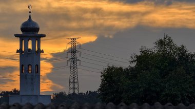 Gün batımında caminin minare silueti dramatik gökyüzü manzarasıyla İslami mimari güç hatlarını ve altın bulutları Din Kültürü ve Şehir Arkaplanı için mükemmel
