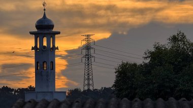 Gün batımında caminin minare silueti dramatik gökyüzü manzarasıyla İslami mimari güç hatlarını ve altın bulutları Din Kültürü ve Şehir Arkaplanı için mükemmel