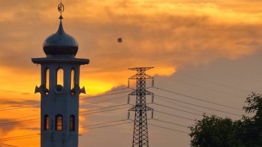 Gün batımında caminin minare silueti dramatik gökyüzü manzarasıyla İslami mimari güç hatlarını ve altın bulutları Din Kültürü ve Şehir Arkaplanı için mükemmel
