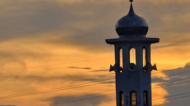 Gün batımında caminin minare silueti dramatik gökyüzü manzarasıyla İslami mimari güç hatlarını ve altın bulutları Din Kültürü ve Şehir Arkaplanı için mükemmel