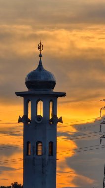 Gün batımında caminin minare silueti dramatik gökyüzü manzarasıyla İslami mimari güç hatlarını ve altın bulutları Din Kültürü ve Şehir Arkaplanı için mükemmel