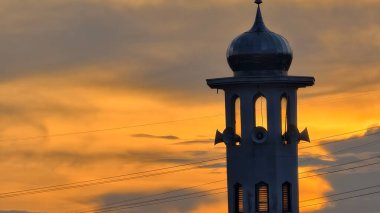 Gün batımında caminin minare silueti dramatik gökyüzü manzarasıyla İslami mimari güç hatlarını ve altın bulutları Din Kültürü ve Şehir Arkaplanı için mükemmel