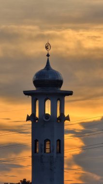 Gün batımında caminin minare silueti dramatik gökyüzü manzarasıyla İslami mimari güç hatlarını ve altın bulutları Din Kültürü ve Şehir Arkaplanı için mükemmel