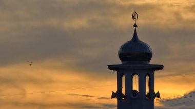 Gün batımında caminin minare silueti dramatik gökyüzü manzarasıyla İslami mimari güç hatlarını ve altın bulutları Din Kültürü ve Şehir Arkaplanı için mükemmel