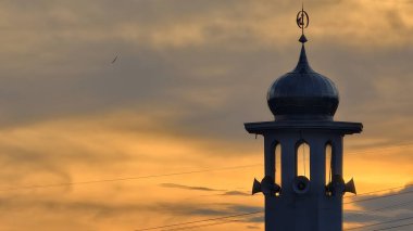 Gün batımında caminin minare silueti dramatik gökyüzü manzarasıyla İslami mimari güç hatlarını ve altın bulutları Din Kültürü ve Şehir Arkaplanı için mükemmel
