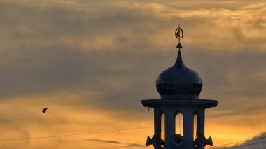 Gün batımında caminin minare silueti dramatik gökyüzü manzarasıyla İslami mimari güç hatlarını ve altın bulutları Din Kültürü ve Şehir Arkaplanı için mükemmel