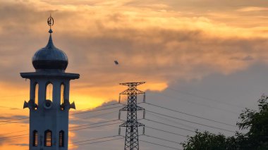 Gün batımında caminin minare silueti dramatik gökyüzü manzarasıyla İslami mimari güç hatlarını ve altın bulutları Din Kültürü ve Şehir Arkaplanı için mükemmel