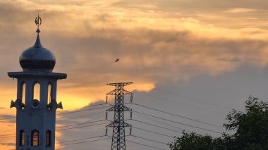 Gün batımında caminin minare silueti dramatik gökyüzü manzarasıyla İslami mimari güç hatlarını ve altın bulutları Din Kültürü ve Şehir Arkaplanı için mükemmel