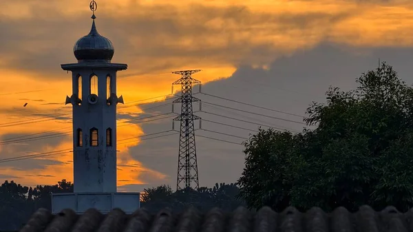 Gün batımında caminin minare silueti dramatik gökyüzü manzarasıyla İslami mimari güç hatlarını ve altın bulutları Din Kültürü ve Şehir Arkaplanı için mükemmel
