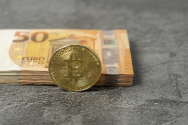 Bitcoin coin next to several euro banknotes on a gray background. Concept of investments in new virtual currencies. Copy Space